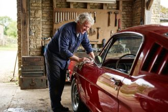 Propriétaire âgé polissant une voiture ancienne rouge des années 60 dans un garage artisanal en pierre, illustration pour assurance auto collection